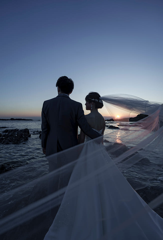 夕暮れの海辺で佇む新郎新婦の後ろ姿